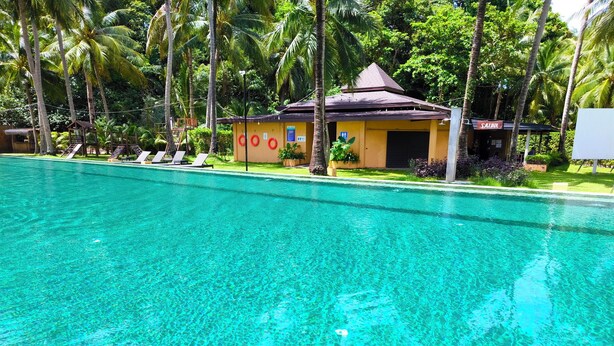 A clear swimming pool with lounge chairs and a small building with a sign that reads 'SAUNA'.