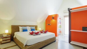 A hotel room with a bed, a nightstand, a lamp, and a bright orange accent wall.