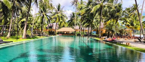 A clear pool surrounded by palm trees and a thatched-roof structure.