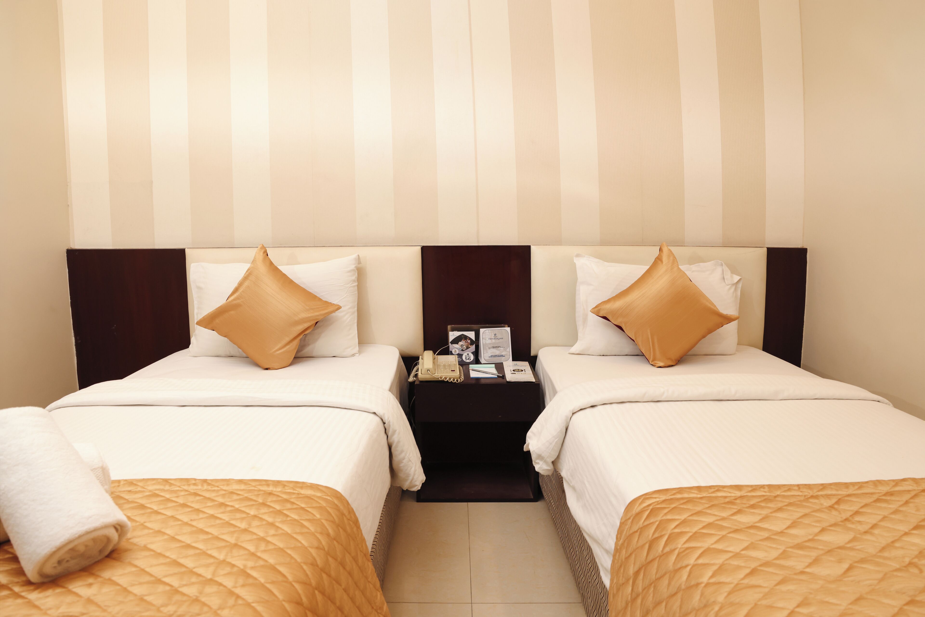 Habitación de hotel con dos camas, una mesita de noche y una pared a rayas.