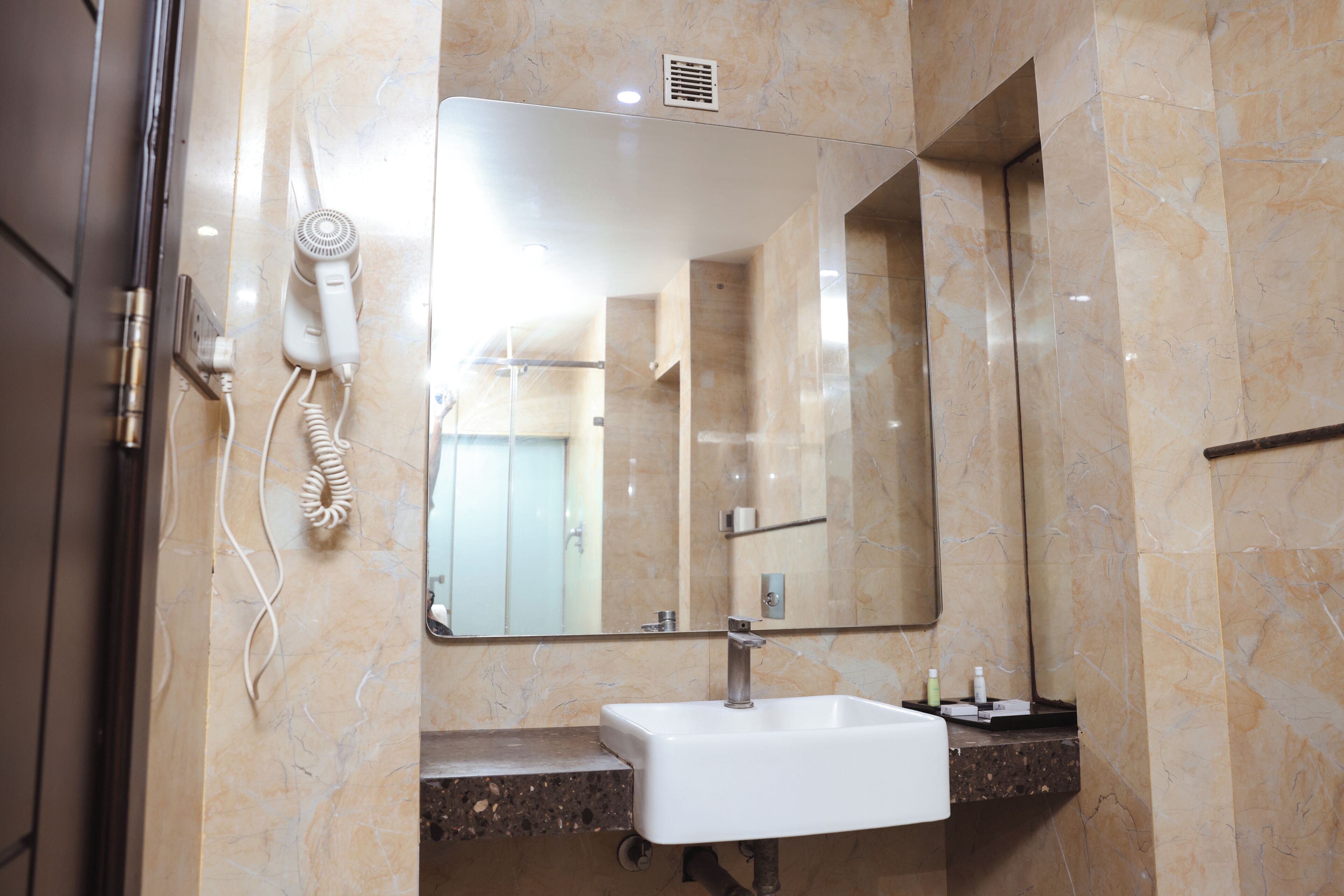 Un bagno con una parete in marmo, un lavandino bianco, uno specchio e un asciugacapelli.
