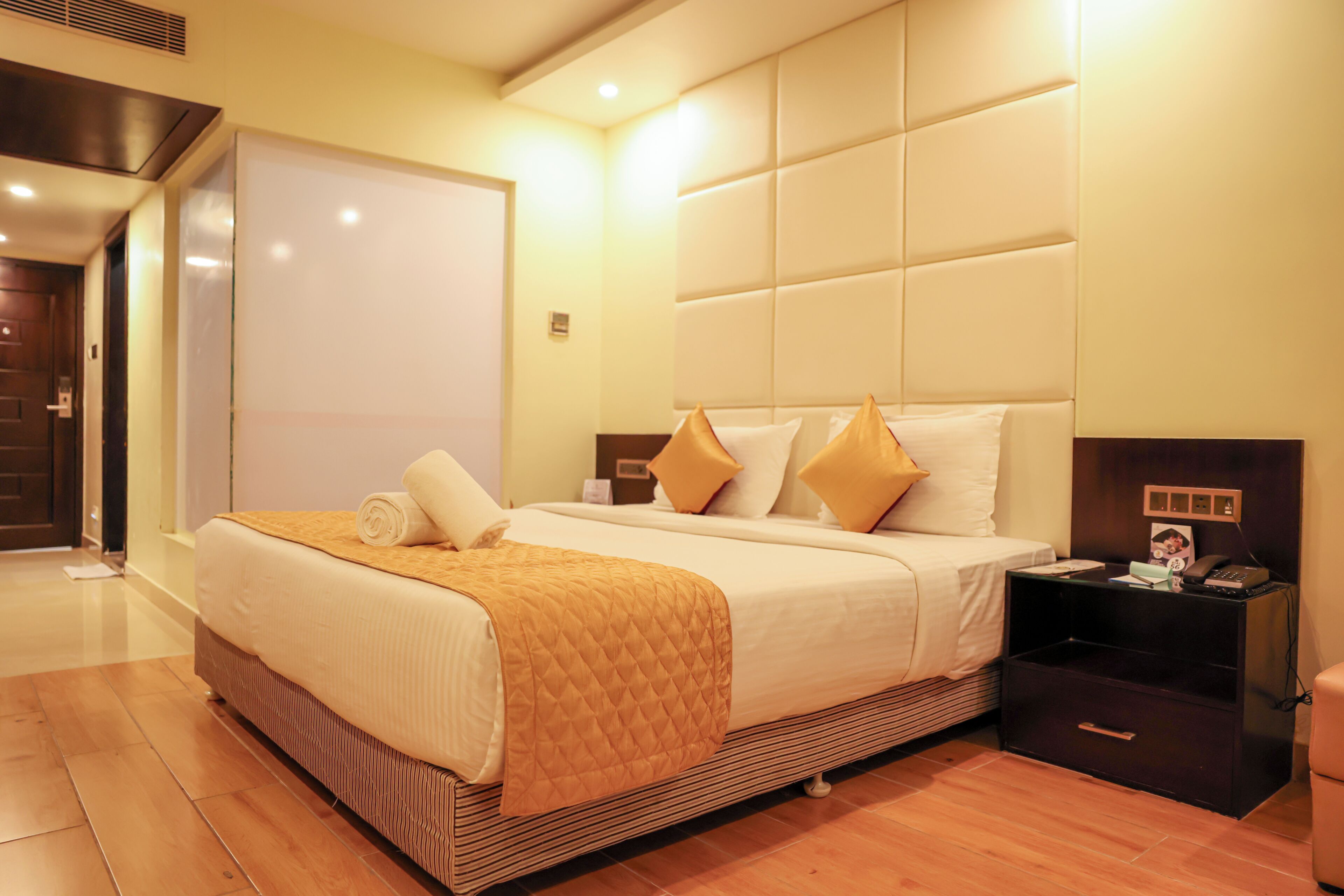 A hotel room with a large bed, a bedside table with a phone and a lamp, and a wooden floor.