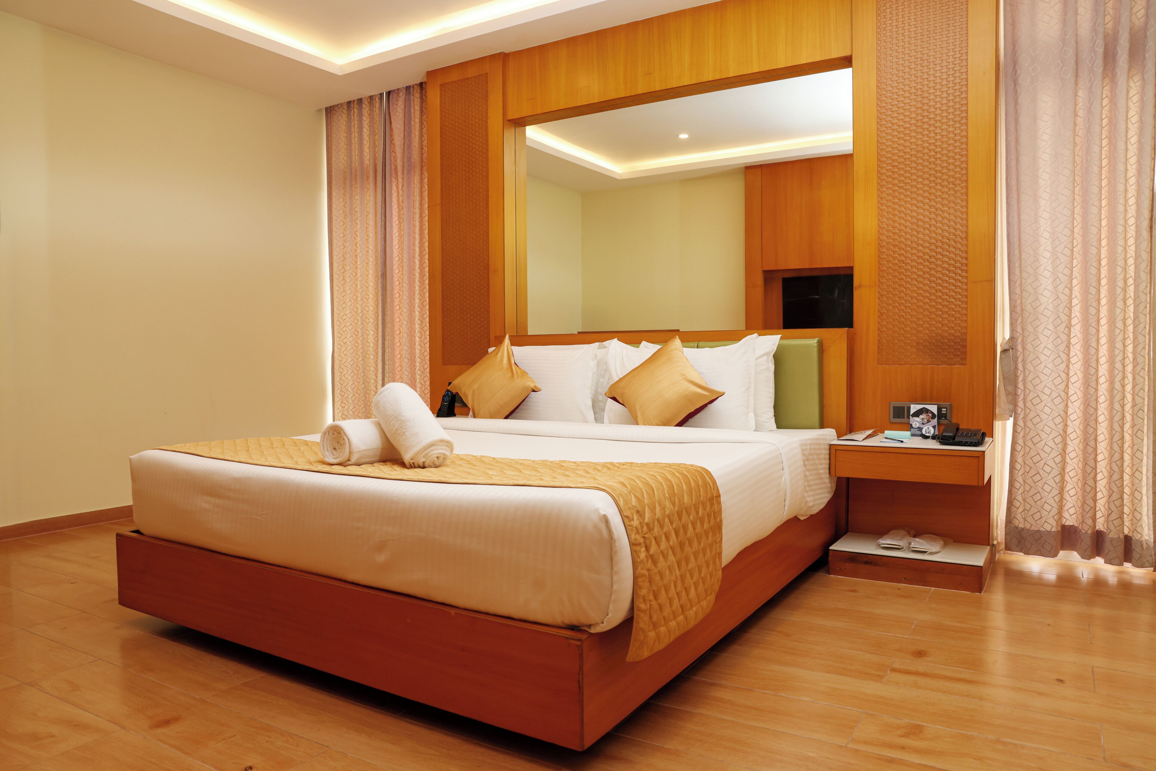 Habitación de hotel con una cama grande, cabecero de madera, una mesita de noche y un espejo.