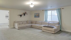 A living room with a sectional sofa, a ceiling light, a map on the wall, and a window with curtains. - Fenced Yard! Family Home on Golf Course in Denver (Denver)