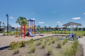 Un parque infantil con toboganes y estructuras de escalada, rodeado de un área ajardinada con césped y arbustos.