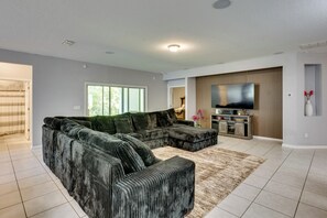 A modern living room with a sectional sofa, a flat-screen TV, and a fireplace. - Orange Park 'The Gathering House' w/ Pool Access (Orange Park)