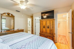 A bedroom with a large bed, a wardrobe, a ceiling fan, and a television. - 'Fifth Gold Tee' Fairway Views, Lanai & Golf Cart! (Lady Lake)