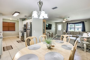 A modern kitchen with stainless steel appliances, a dining area with a wooden table and chairs, and a living room with a sofa and a television. - 'Fifth Gold Tee' Fairway Views, Lanai & Golf Cart! (Lady Lake)