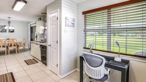 Une cuisine moderne avec un coin repas, un bureau avec un ordinateur et une chaise, ainsi qu’une fenêtre équipée de stores.