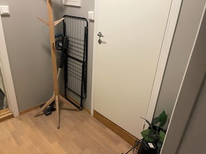 Et værelse med trægulv, en dør med håndtag, et sort metalstativ og en potteplante.