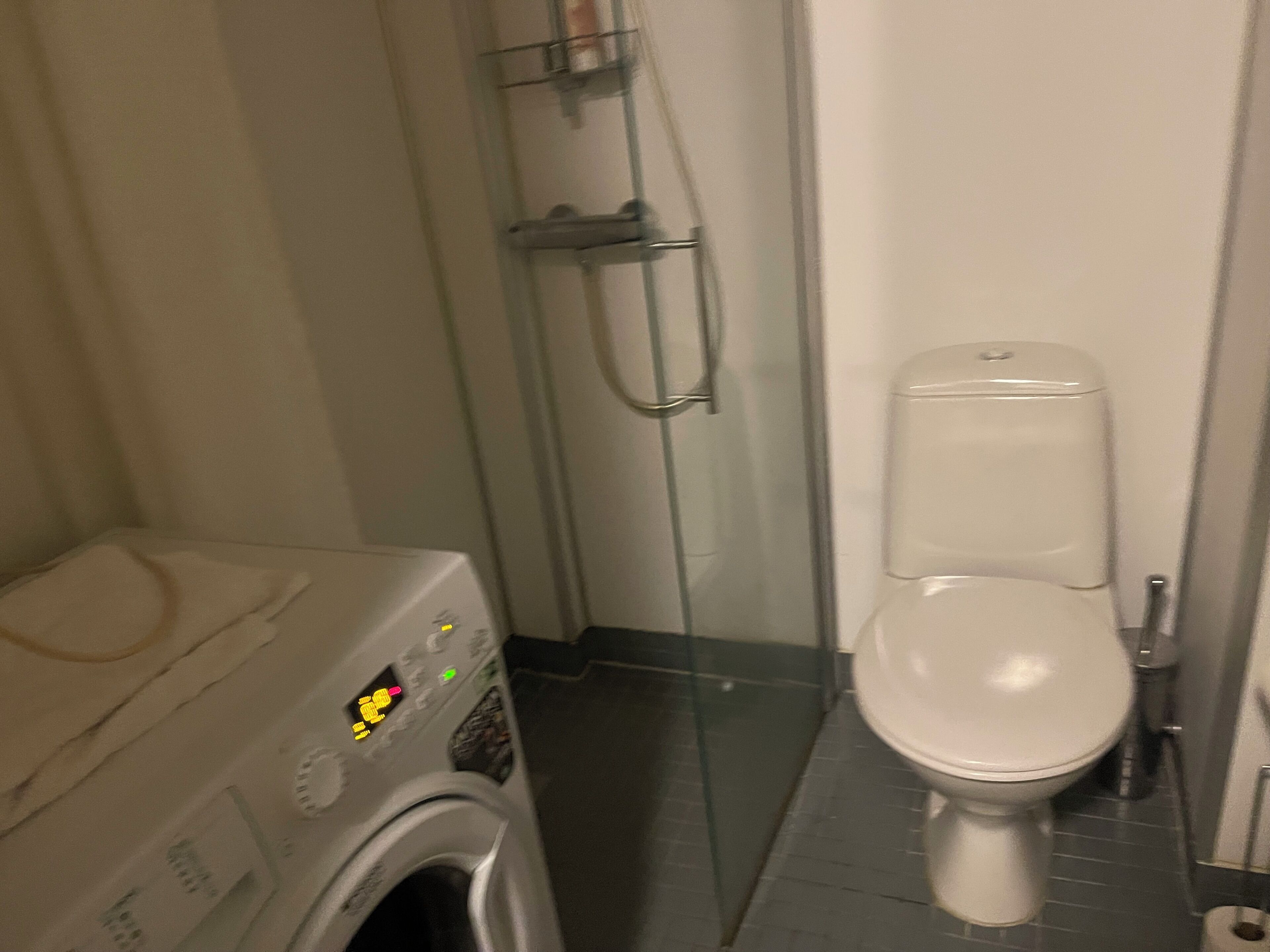 Een kleine badkamer met een wasmachine, toilet en douchecabine.