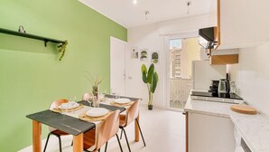 Un coin repas avec une table dressée pour quatre personnes, une cuisine équipée d’un four à micro-ondes et d’une bouilloire, et un mur végétal.