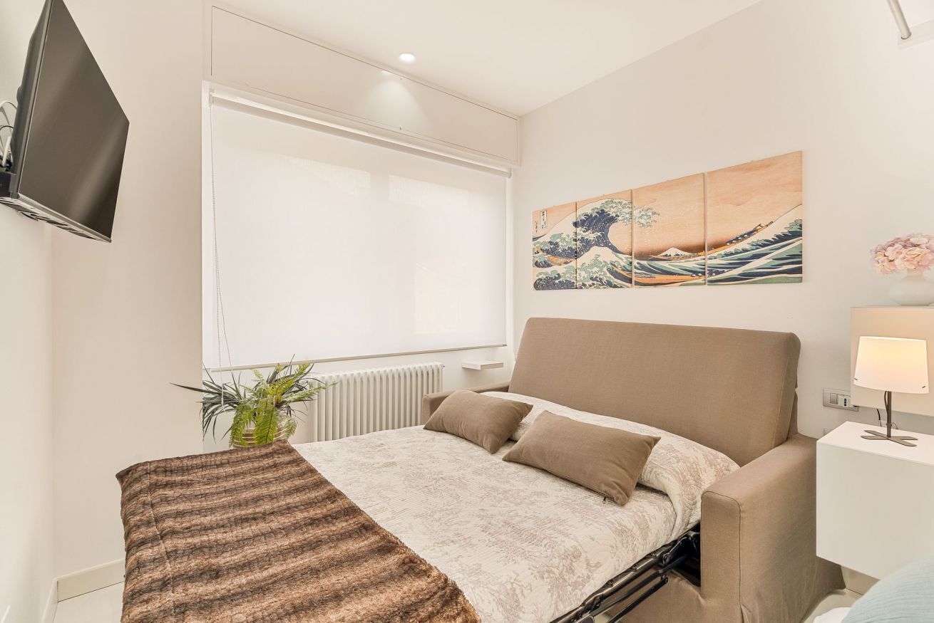 A modern bedroom with a bed, a television mounted on the wall, and a painting above the bed.