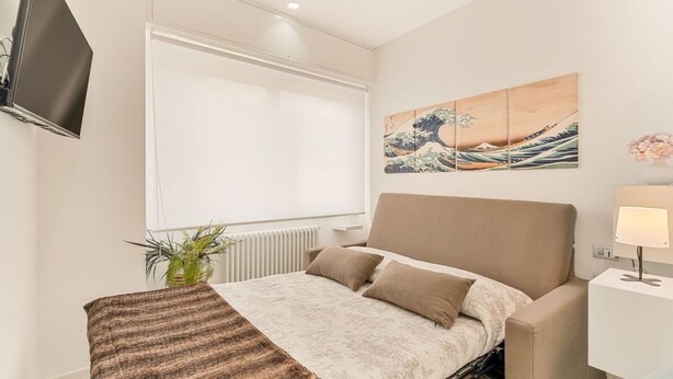 Une chambre à coucher moderne avec un lit, un téléviseur fixé au mur et un tableau au-dessus du lit.