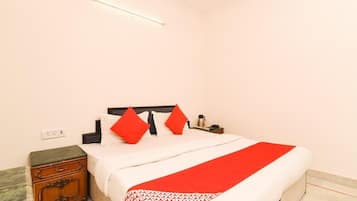 Habitación de hotel con cama, mesita de noche, lámpara y toma de corriente.