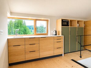 A modern kitchen with wooden cabinets, a built-in microwave, and a window overlooking greenery.