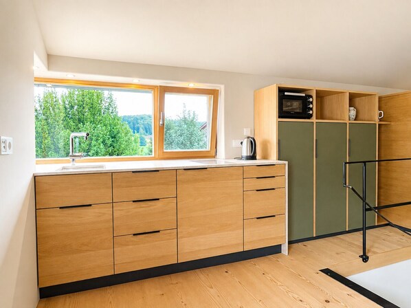 A modern kitchen with wooden cabinets, a built-in microwave, and a window overlooking greenery.