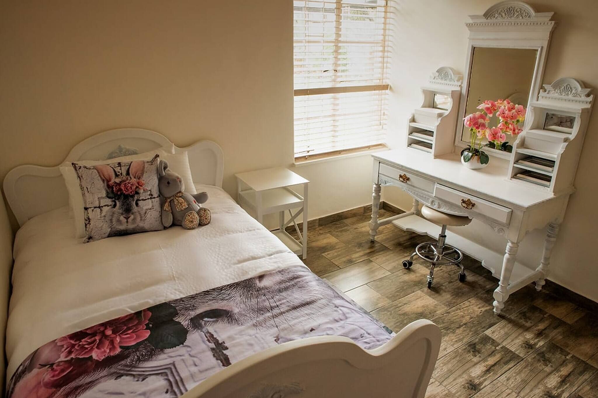 A bedroom with a bed, a dresser, a vanity, and a window with blinds.