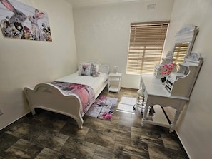 Ein Schlafzimmer mit Bett, Nachttisch, Schminktisch, Spiegel, Fenster und einem Wandbild.
