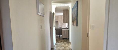 A hallway with wooden flooring leading to a kitchen area.