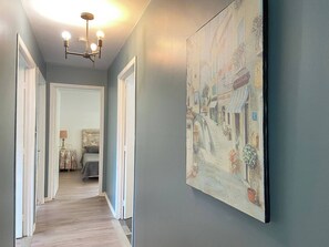 Un couloir orné d’un tableau représentant une scène de rue, d’un lustre et, au fond, d’un lit.