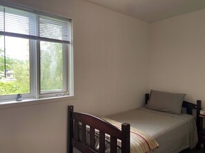 Une petite chambre avec un lit simple, une fenêtre, une chaise et une table de chevet.