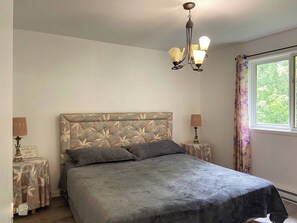 Une chambre à coucher avec un lit, un lustre, une fenêtre avec des rideaux et deux tables de chevet avec des lampes.