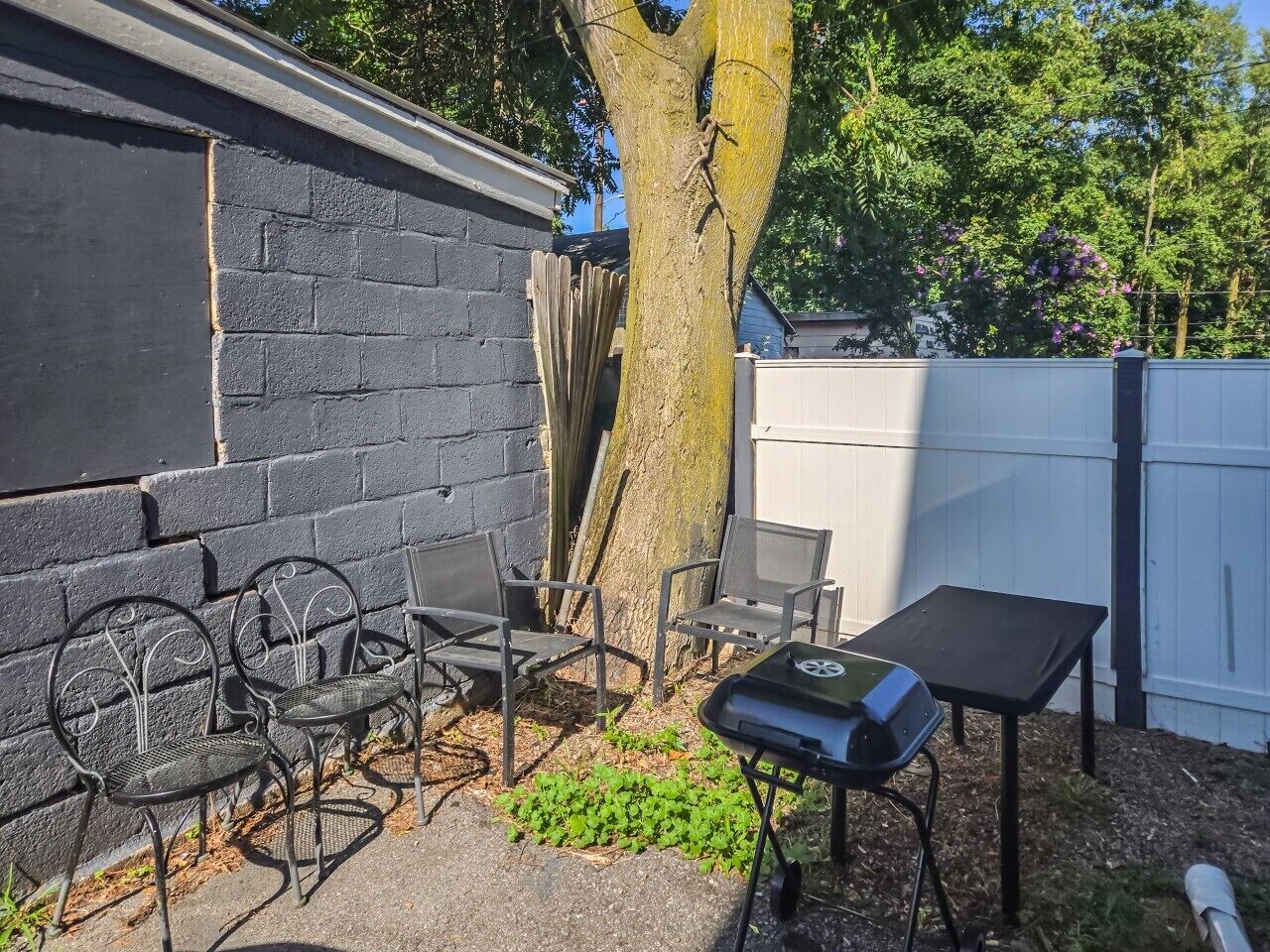 A patio area with a grill, metal chairs, and a table.