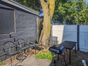 A patio area with a grill, metal chairs, and a table. - Seward Street - Room 5 (Rochester)