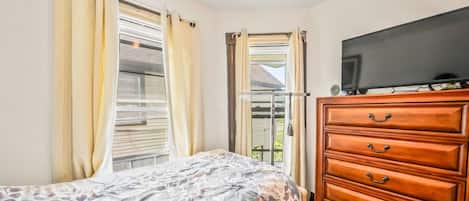 A bedroom with a bed, a wooden dresser, a television, and a window with curtains.