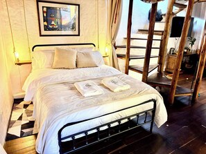 A bed with a metal frame, white bedding, and two towels on the bed. There is a painting on the wall above the bed. - iECHIE Historic Colonial Stay in La Candelaria (Bogotá)