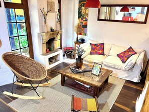 A cozy living room with a wicker chair, a sofa with colorful pillows, a coffee table with a vase and picture frame, and a fireplace with decorative items. - iECHIE Historic Colonial Stay in La Candelaria (Bogotá)