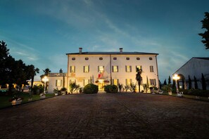 A large, multi-story building with a symmetrical facade, a central entrance with a flag, and a paved courtyard.