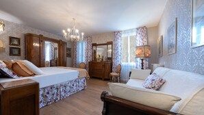 Ein Schlafzimmer mit einem Bett, einem Sofa, einem Schminktisch, einem Sessel und einem Spiegel.
