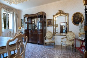 A room with a dining table, chairs, a cabinet with glass doors, a mirror with an ornate frame, and a painting on the wall.