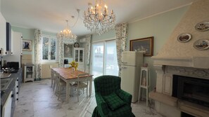 A dining area with a chandelier, a table with chairs, a refrigerator, and a fireplace.