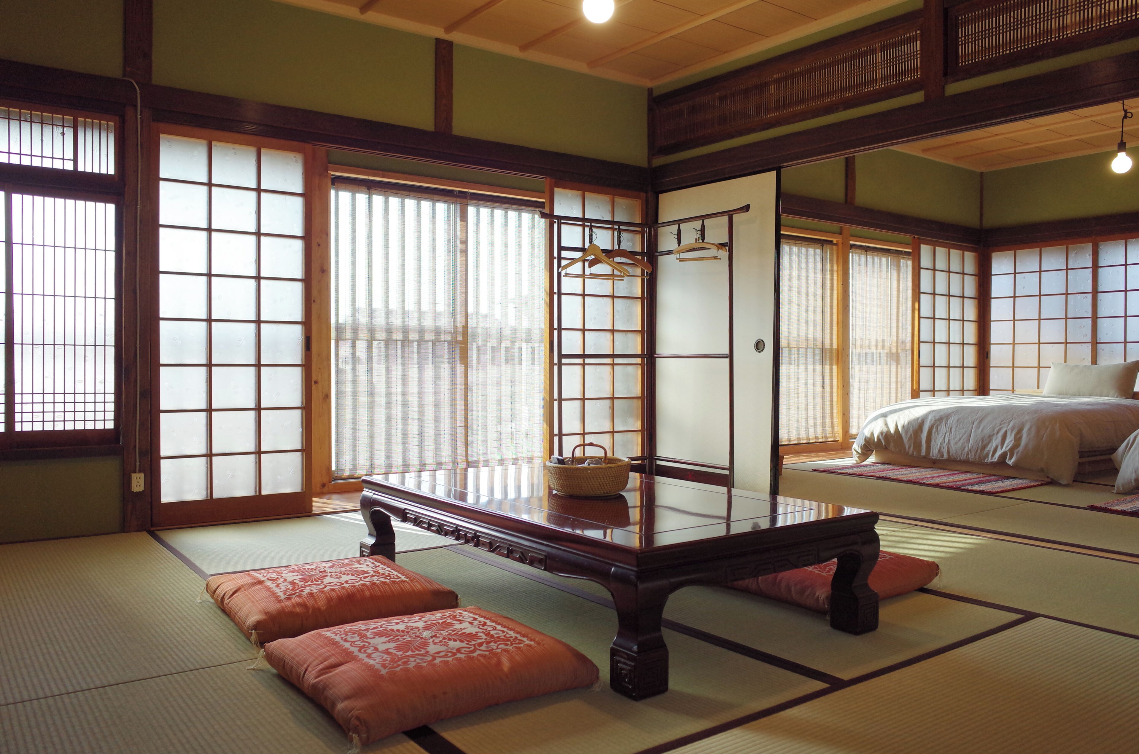 A traditional Japanese room with tatami flooring, a low wooden table, and a bed with a white bedspread.