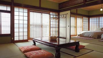 A traditional Japanese room with tatami flooring, a low wooden table, and a bed with a white bedspread.