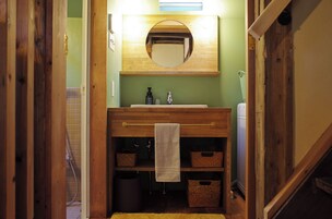 Un baño con tocador de madera, espejo, toalla colgando en un perchero y cestas de almacenamiento.