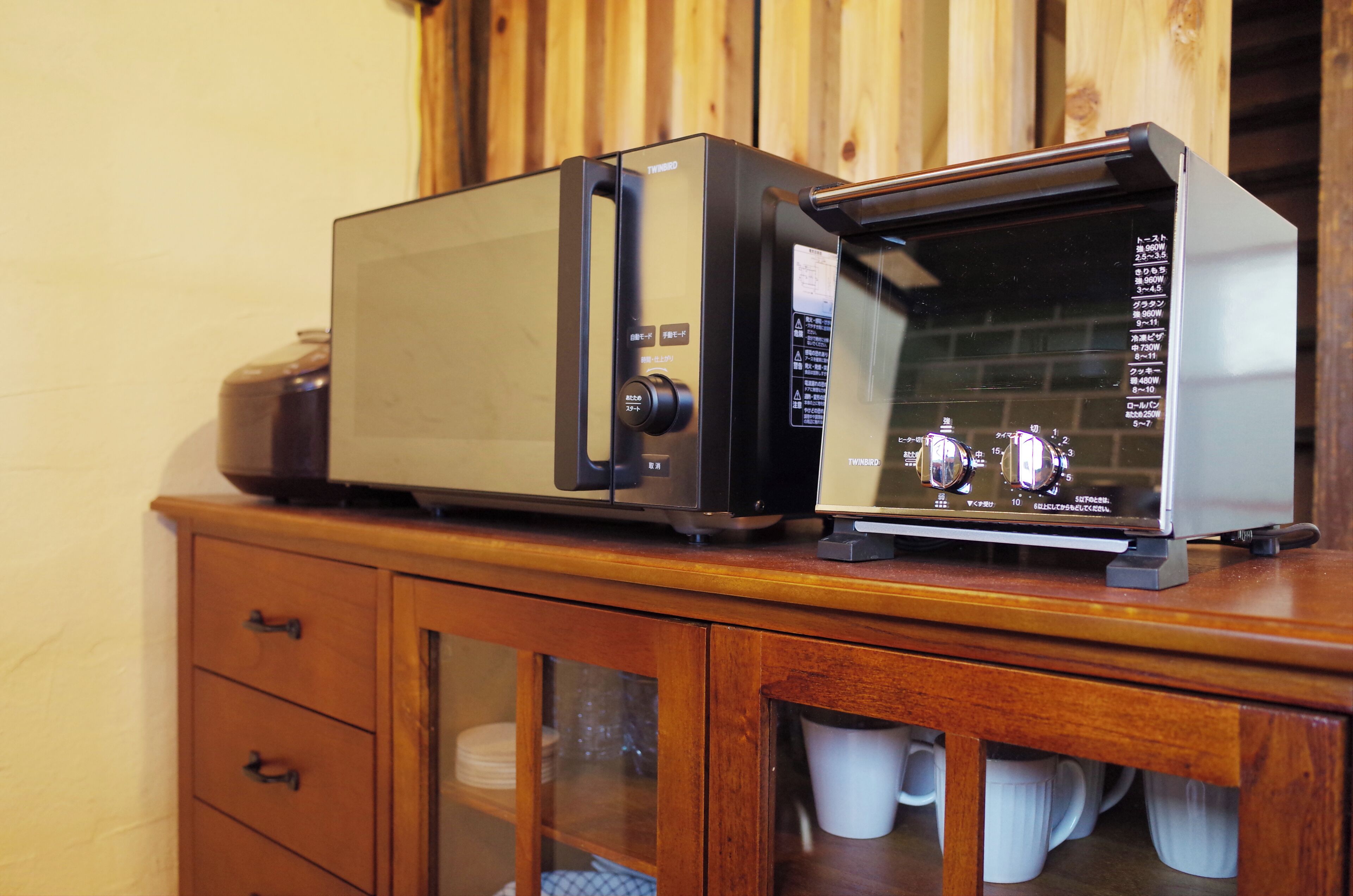 A microwave oven on a wooden cabinet with drawers and a glass-fronted cabinet below.