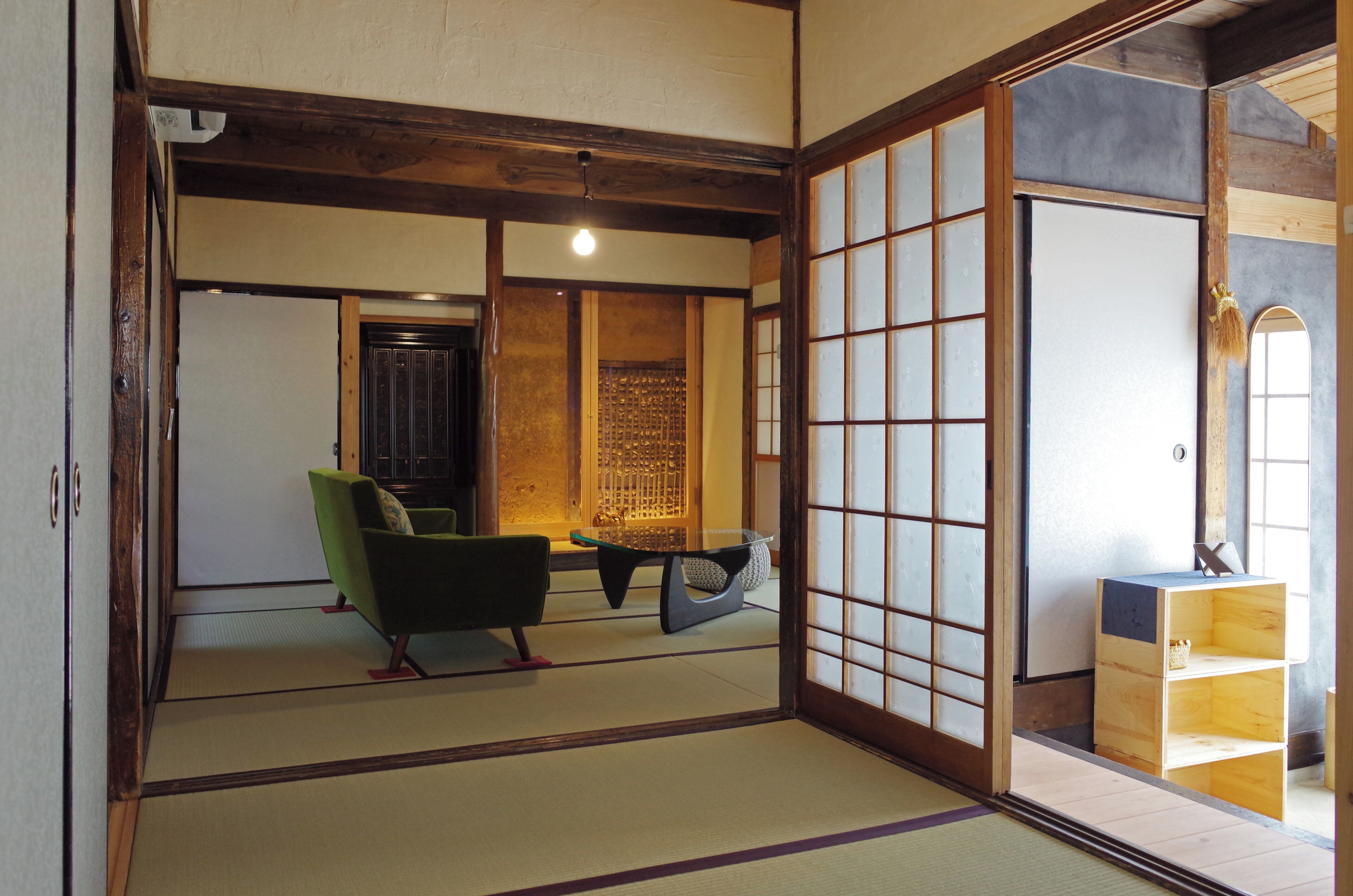 A traditional Japanese room with tatami flooring, a green chair, a low table, and a sliding door with frosted glass panels.