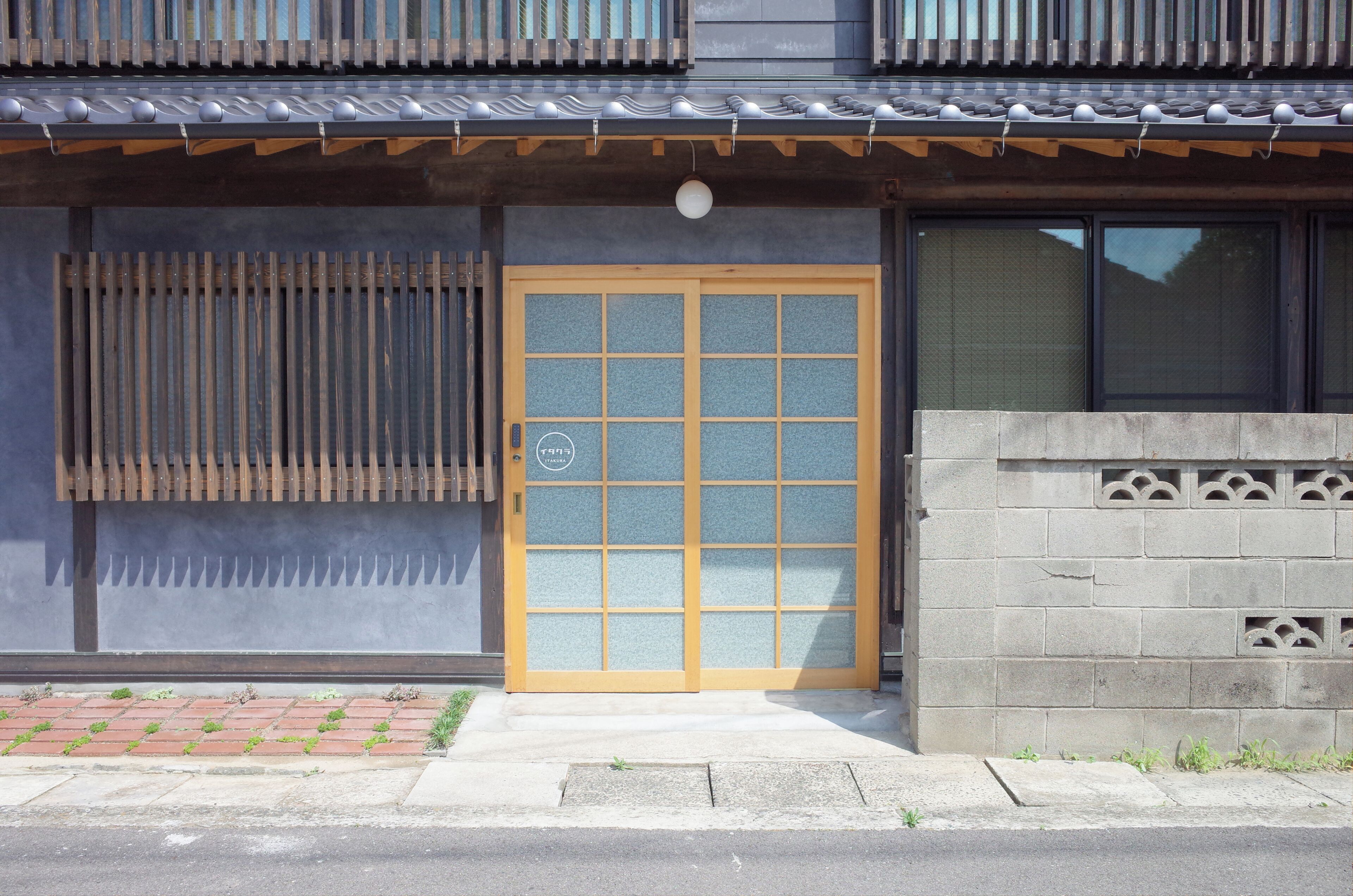 Ein traditionelles japanisches Gebäude mit einer Holztür, einem Schiebeglasfenster und einem Ziegeldach.