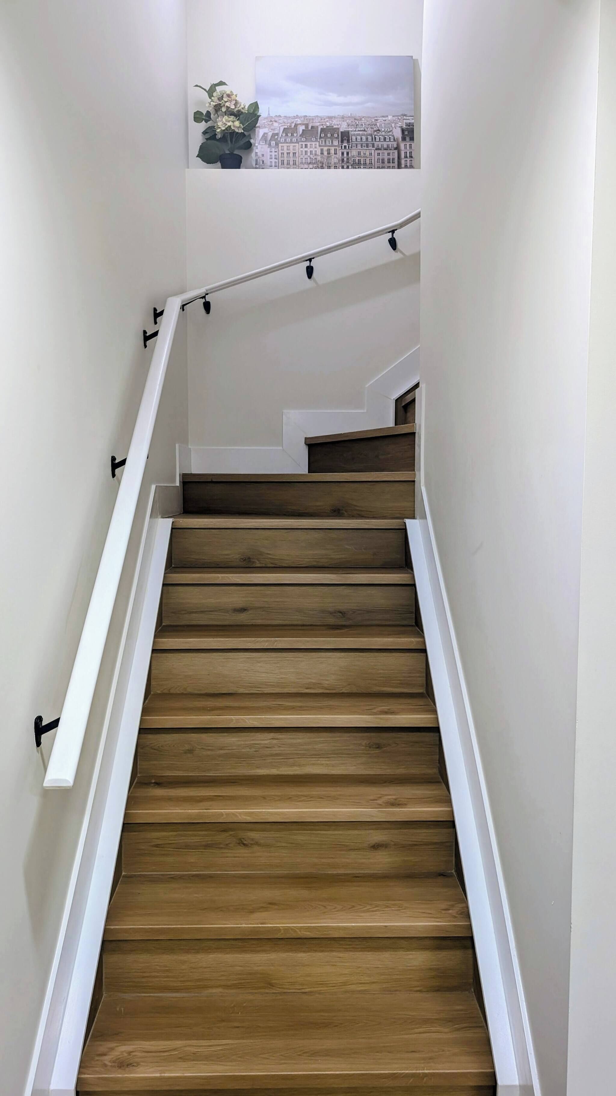 A wooden staircase with white walls and a cityscape painting above.