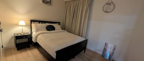 Una cama bien hecha con cabecera, una mesita de noche con lámpara, y una pared con un cuadro enmarcado y una frase motivacional.