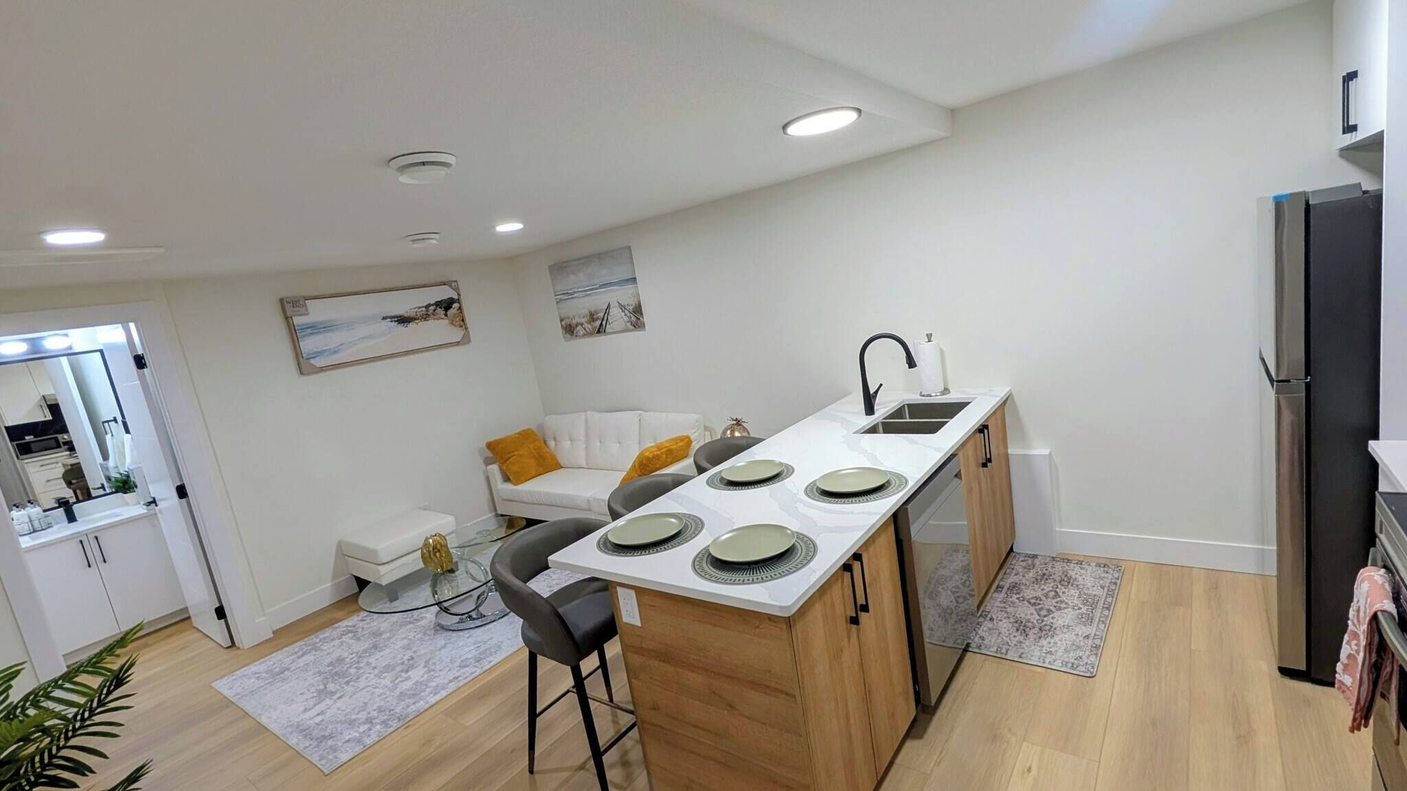 A modern kitchen with a central island, white cabinetry, and a dining area with a white sofa and a small table.