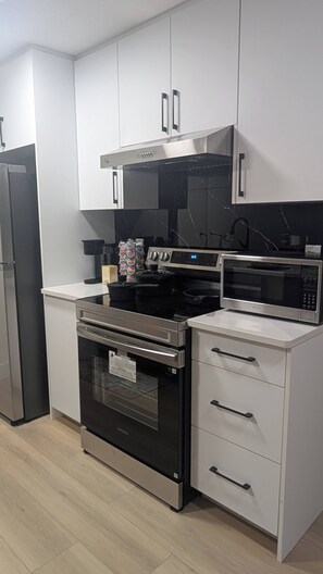 A modern kitchen with stainless steel appliances, white cabinetry, and a black countertop.