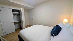 A hotel room with a bed, a bedside lamp, and a wardrobe with hanging clothes.