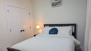 A bedroom with a bed, a nightstand, a lamp, a door, and a ceiling light.