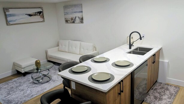 A compact kitchen with a white countertop, four plates, a sink, and a small dining area with a glass table and chairs.