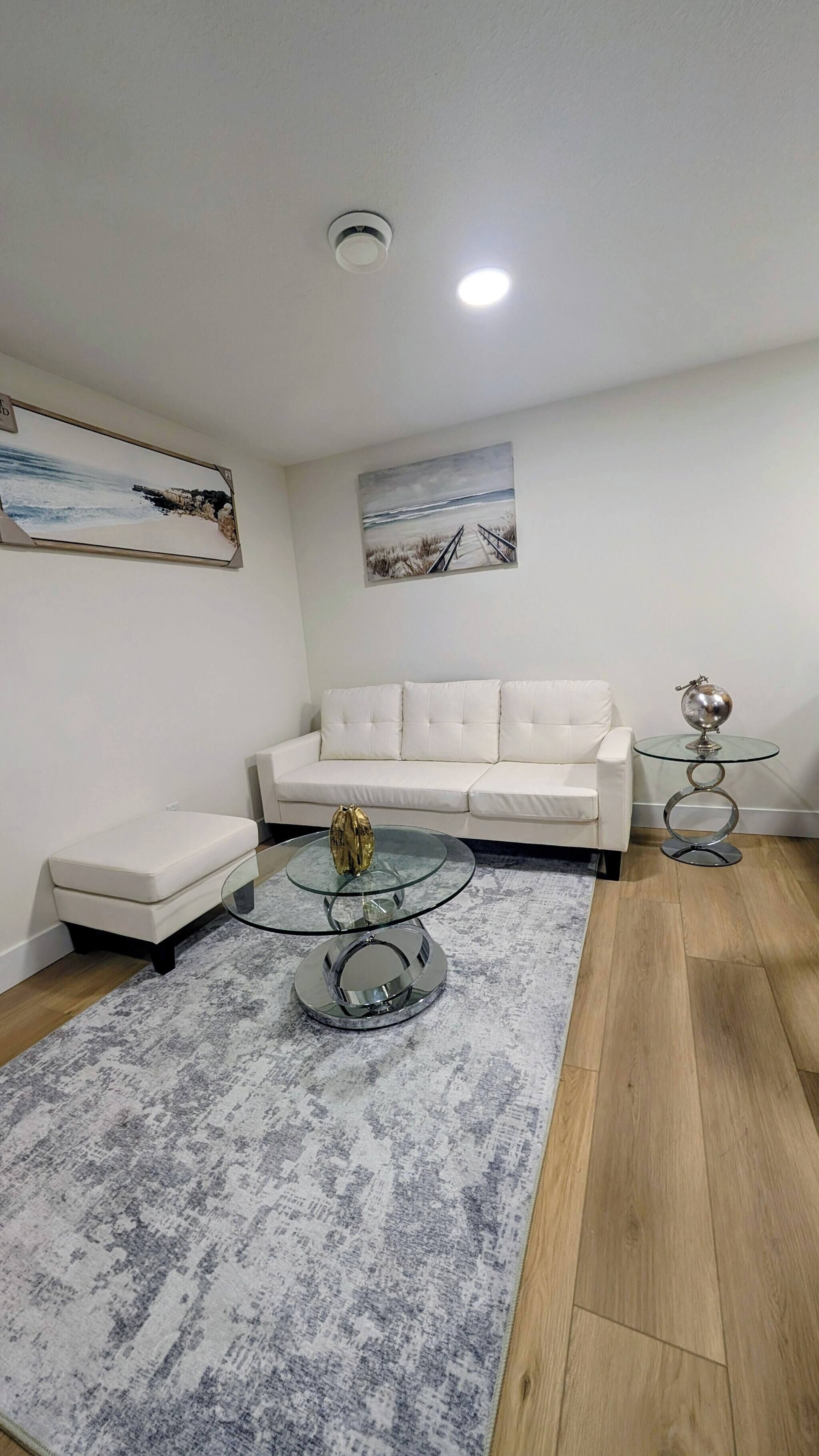 A modern living room with a white sofa, a glass coffee table, and a patterned rug.